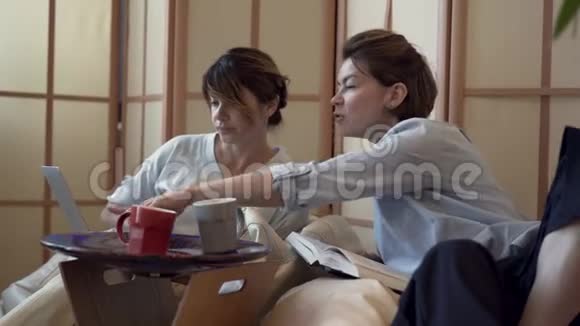 两个成年妇女一起在家里喝茶或喝咖啡一起在笔记本电脑上看电影两个优雅成熟的女朋友视频的预览图