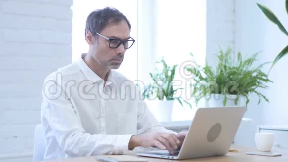 是的中年男子在笔记本电脑上工作时摇头接受提议视频的预览图