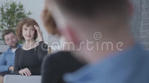 可爱的年长成熟的女人照镜子看着她的倒影抚摸着她坐在年轻人面前的头发视频的预览图