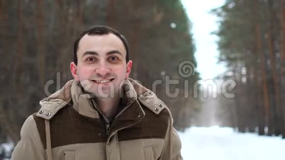 穿着夹克衫的年轻人的画像笑得满脸幸福人站在冬林中视频的预览图