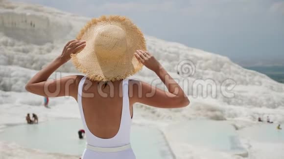 穿着白色泳衣和草帽的女人站在白色的山上视频的预览图
