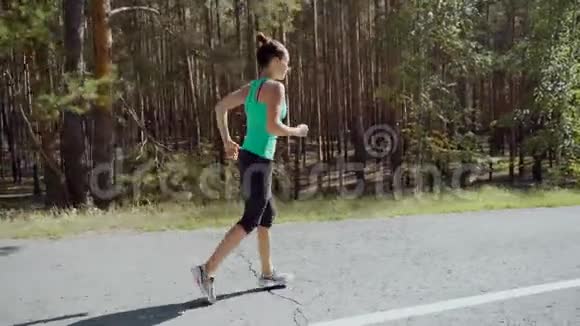 早上在乡村公路上跑步的年轻运动员的侧视镜头美丽的白种人女运动员在阳光明媚的夏天视频的预览图