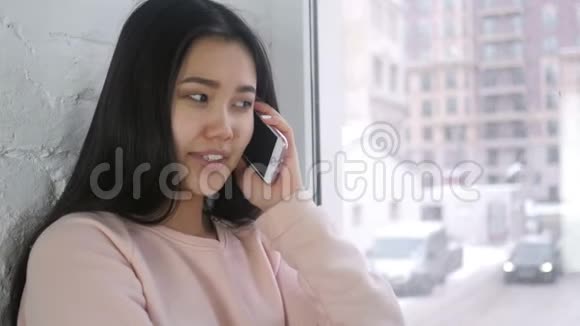 年轻的亚洲女人在智能手机上聊天坐在窗边视频的预览图