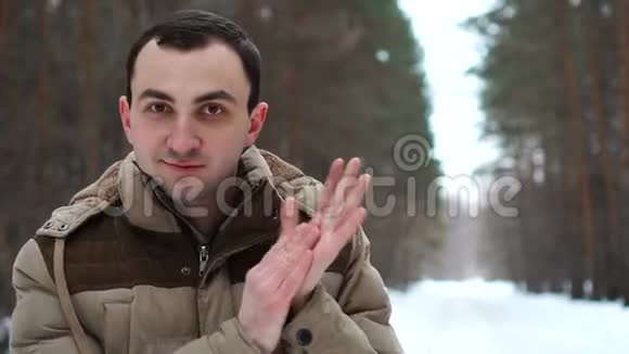 穿夹克的年轻人的肖像在户外鼓掌人站在冬林中视频的预览图
