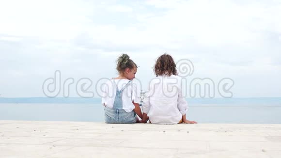 两个孩子一个男孩和一个女孩坐在亚得里亚海的岸边欣赏一艘经过的船夏季视频的预览图