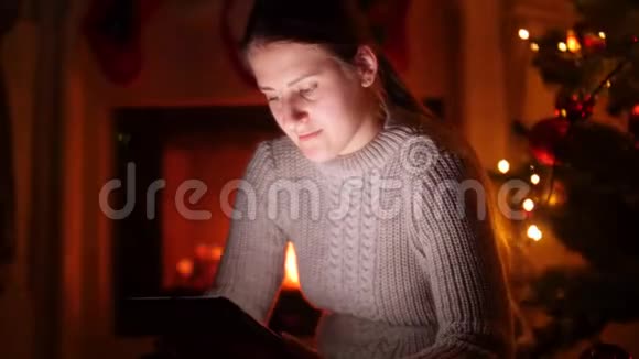 4k视频一位年轻女子她拿着数码平板电脑坐在圣诞树旁视频的预览图