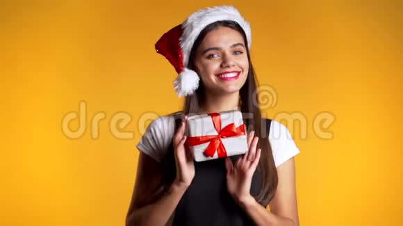 年轻可爱的女孩微笑着拿着礼物盒在黄色的工作室背景视频的预览图