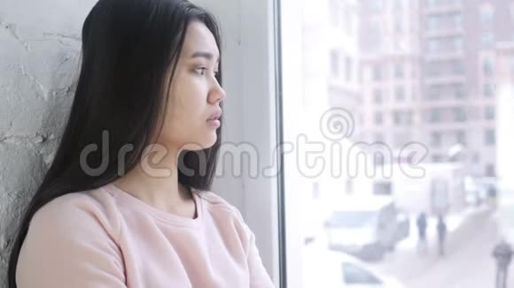 伤心难过的年轻亚洲女人坐在窗前视频的预览图