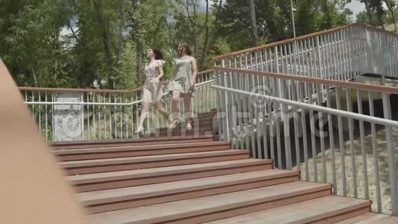 两个穿着夏装的漂亮女孩在城市公园的楼梯上奔跑无忧无虑的女朋友玩得开心视频的预览图