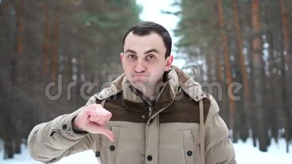 穿夹克的人的肖像显示拇指向下人站在冬林中视频的预览图