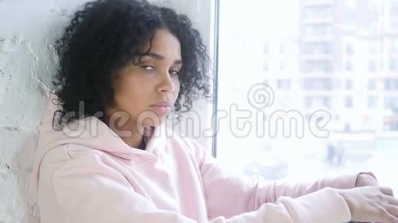 年轻的非洲女人指着相机坐在窗前视频的预览图