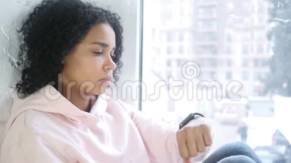 黑人妇女坐在窗前等待和观看时间视频的预览图