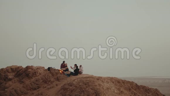 一群朋友在日落时分在山顶上放松坐在篝火旁享受他们的时光友谊青春视频的预览图