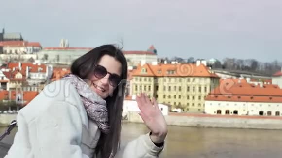 中镜头微笑优雅的女游客挥舞着手看着站在城市堤上的摄像机视频的预览图