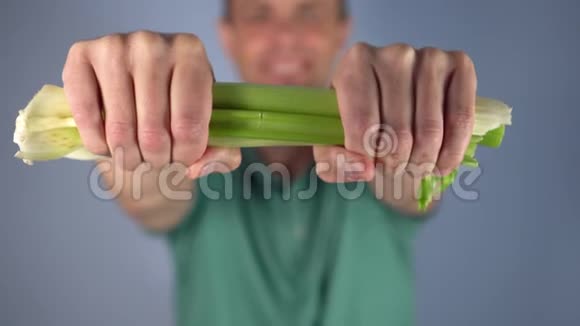 一个穿绿色T恤的人在蓝色背景上打碎了一串芹菜视频的预览图