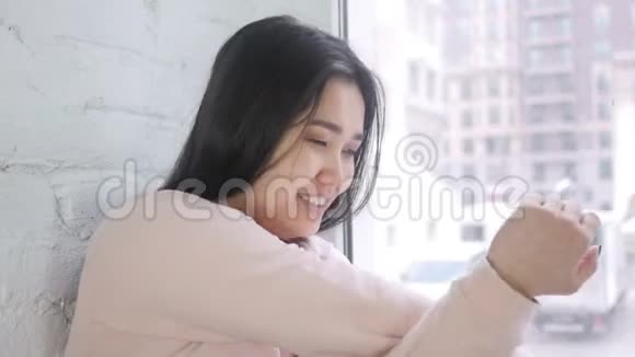 坐在窗前放松的年轻亚洲女人视频的预览图
