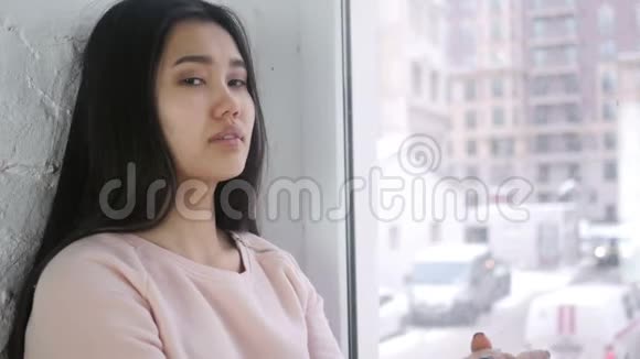年轻的亚洲女人指着相机坐在窗前视频的预览图