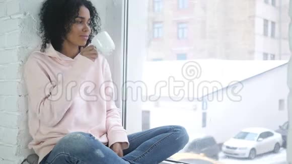 年轻的美国黑人妇女喝咖啡在窗口放松视频的预览图