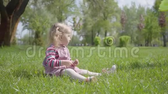 可爱的小女孩坐在公园的草地上独自玩耍用一根小小的手指指向上面无照料儿童休息视频的预览图