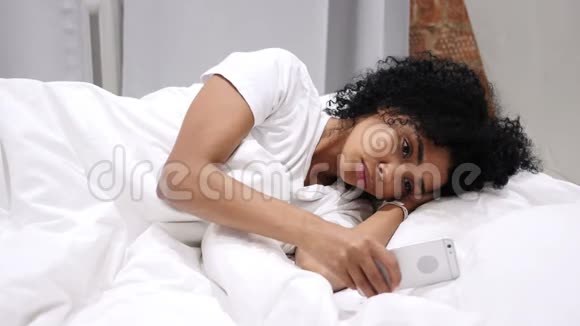 美国黑人女性在智能手机浏览电子邮件和信息躺在床上视频的预览图