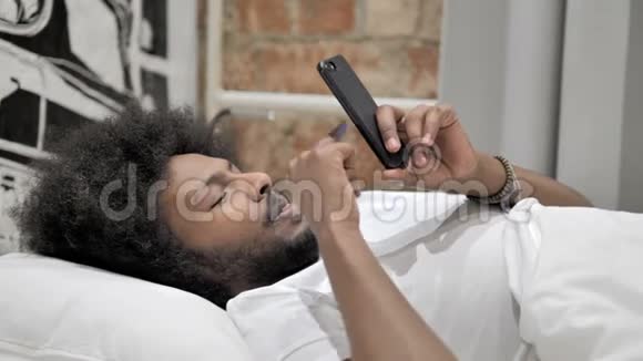 非洲男人使用智能手机躺在床上视频的预览图
