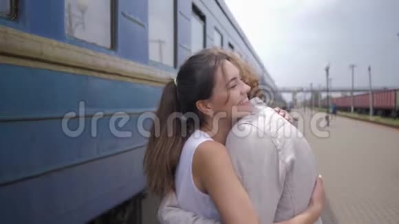 幸福的年轻女子拥抱男人分离后在火车站的火车车厢旁欢笑视频的预览图