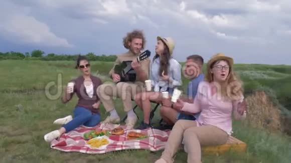 野餐和快乐的朋友在一起男孩和女孩弹吉他唱歌而大自然在河边娱乐视频的预览图