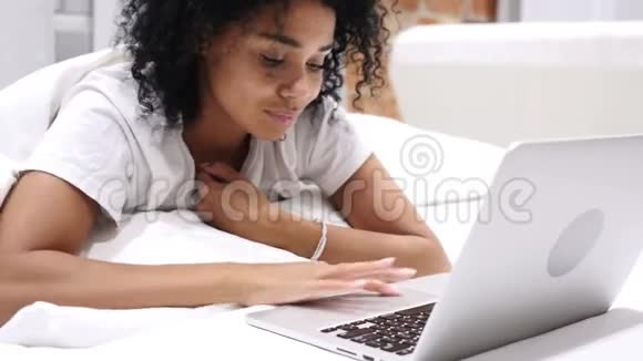 兴奋的美国黑人妇女趴在床上在线视频聊天视频的预览图