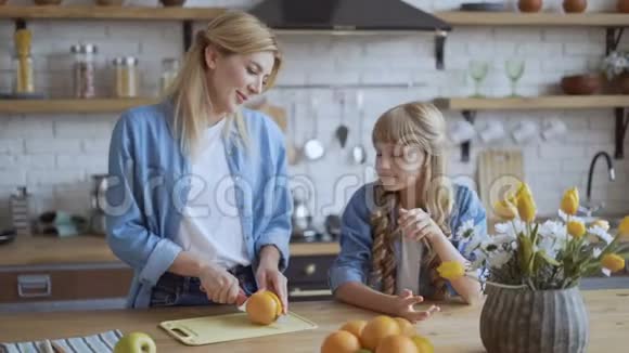 妈妈给女儿切了一个大的多汁橘子幸福的家庭在他们明亮的大家庭的餐厅里4K视频的预览图