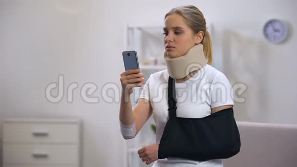 戴泡沫颈项圈和手臂吊带的悲伤女性智能手机阅读信息视频的预览图