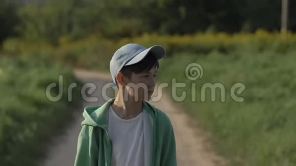 戴着帽子的快乐男孩走在乡间小路上在户外微笑视频的预览图