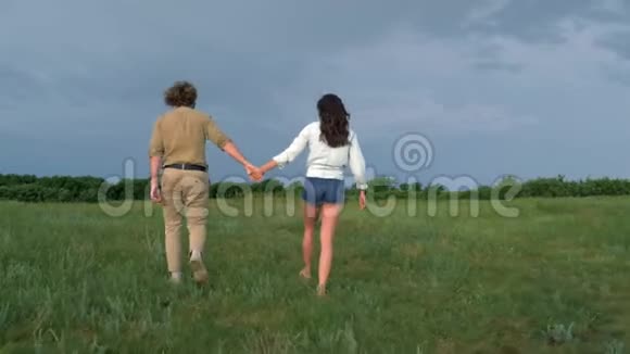 快乐的年轻人和一个相爱的女孩在海玛纳亚的天气里在绿色的草地上散步得开心视频的预览图