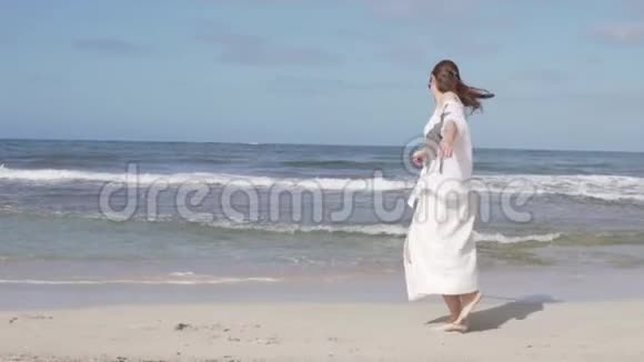 一个快乐的女人在慢慢地旋转把手臂举到海滩上视频的预览图