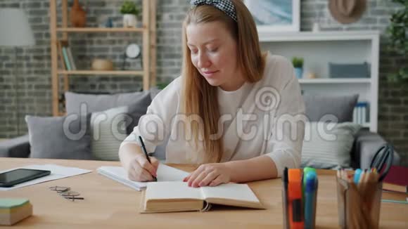 年轻的女学生在办公桌上写着笔记本在家工作视频的预览图