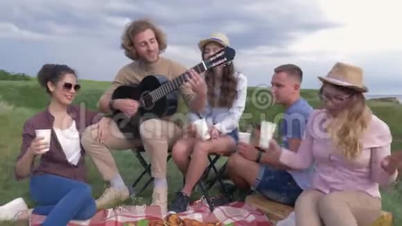 野餐派对有趣的朋友和女朋友在海边休息时玩吉他视频的预览图