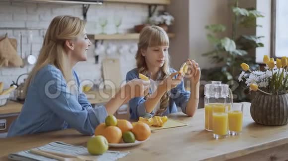 妈妈和女儿坐在餐厅里吃橘子妈妈给一个女孩洗橘子幸福家庭概念4K视频的预览图