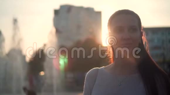 年轻的女人在夕阳的光线下在喷泉和城市景观的背景下喷泉喷水和日落视频的预览图
