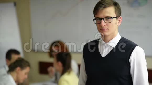 在小办公室里和其他背景的工作人员合拢戴眼镜和法兰绒衬衫的年轻英俊的工人视频的预览图
