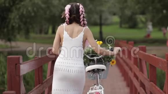 穿着白色夏装的浪漫性感女孩骑着自行车在森林公园的木桥上散步视频的预览图