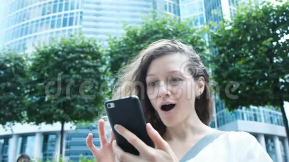女人深情地看着电话在摩天大楼的背景下的惊喜视频的预览图