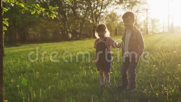 日落时分小男孩和小女孩牵着手在草地上奔跑视频的预览图