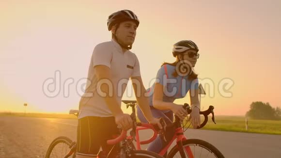 一对戴着自行车头盔的男人和女人在日落时站着说话在公路上骑自行车后休息轨道自行车视频的预览图