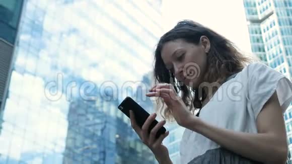 在商业摩天大楼的背景下女孩用智能手机在街道上输入文字视频的预览图