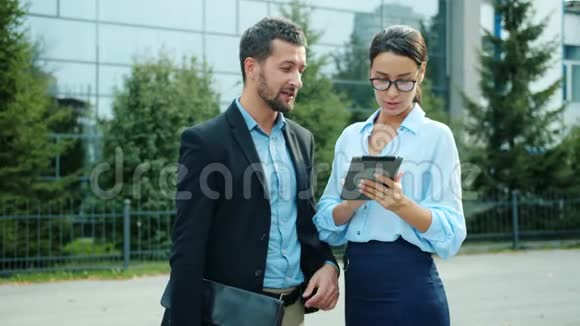 成功的男人和女人在户外使用平板电脑谈论生意视频的预览图