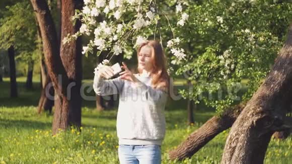 一个美丽的白人女孩在一棵开花的树上自拍整理她的头发视频的预览图