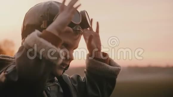 小快乐男孩穿着有趣的老飞行员服装戴着复古航空眼镜在日落场上做着愚蠢的表情慢动作视频的预览图
