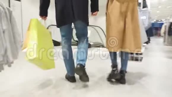 一对年轻的白种人夫妇带着购物袋站在自动扶梯上微笑视频的预览图