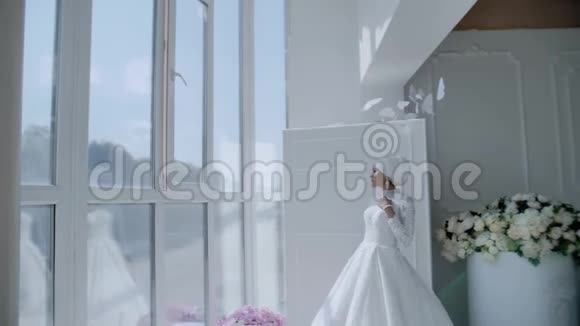 一个美丽美丽的女孩穿着雪白的连衣裙站在一个大的灯光窗口她漂亮极了一个非凡的人物视频的预览图
