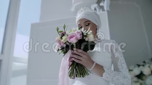 一个美丽的年轻女孩穿着一件全国性的白色连衣裙站在一扇轻窗旁捧着一束花看着视频的预览图