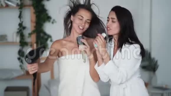 两个穿着白色浴袍跳舞的女朋友带吹风机唱歌和干头发笑吧视频的预览图
